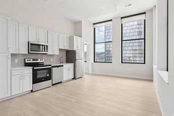 A kitchen with white cabinets and appliances, a wooden floor, and a view of the city through the windows. at LiveWell Apartments, Pittsburgh, PA